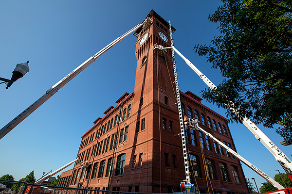 Workers in lifts repair bricks more than 100 feet up on the Clock Tower. The project includes putting a new copper roof on the tower.
