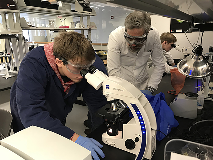 Mykiah Young looks for red and white bloods through a microscope at UW-Stout, as Colfax High School science teacher Mark Mosey looks on.