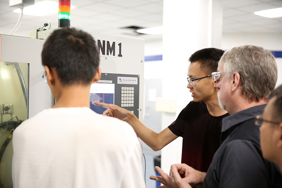 Instructor Paul Craig shows Beijing students how to use a computer numerical control machine in the UW-Stout Fryklund Hall machining lab.