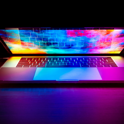 Laptop with a vibrant colorful screen casting blue, pink, and orange light across the keyboard against a dark background