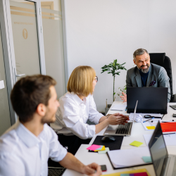 Three professionals collaborating in a bright office workspace, with laptops and materials on the desk.
