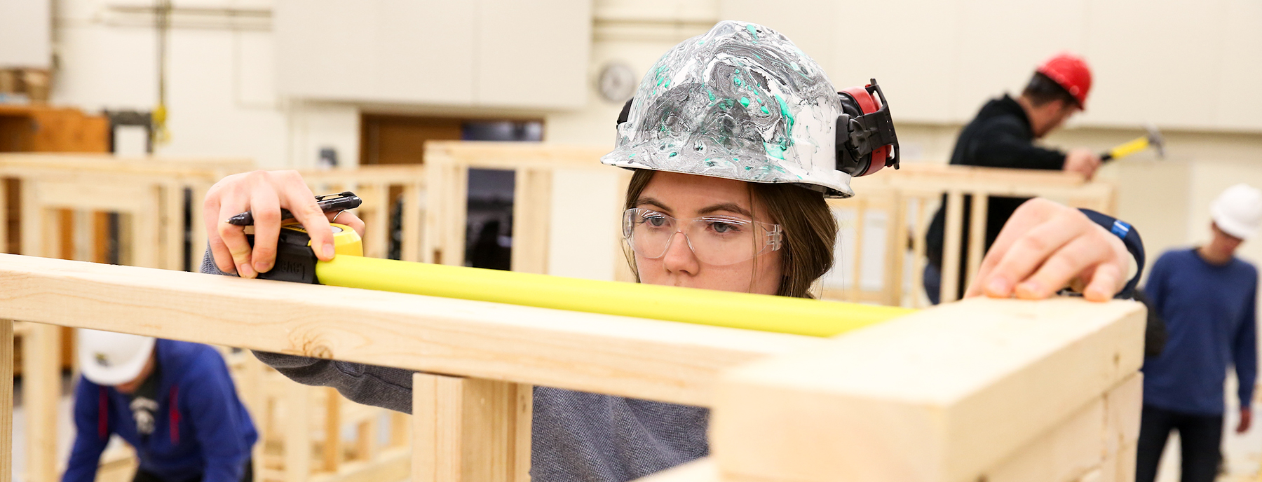 UW-Stout student wears safety equipment and measures project in the Construction Lab.