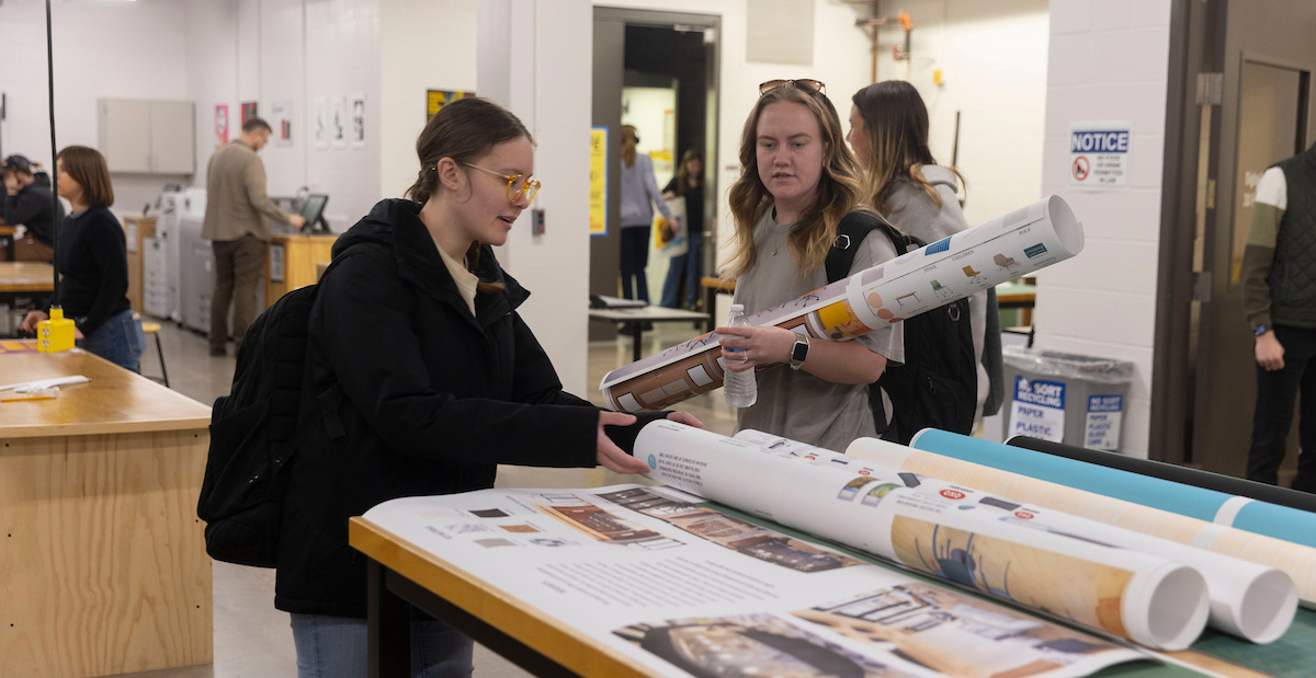 Female students review large format prints for a class project.