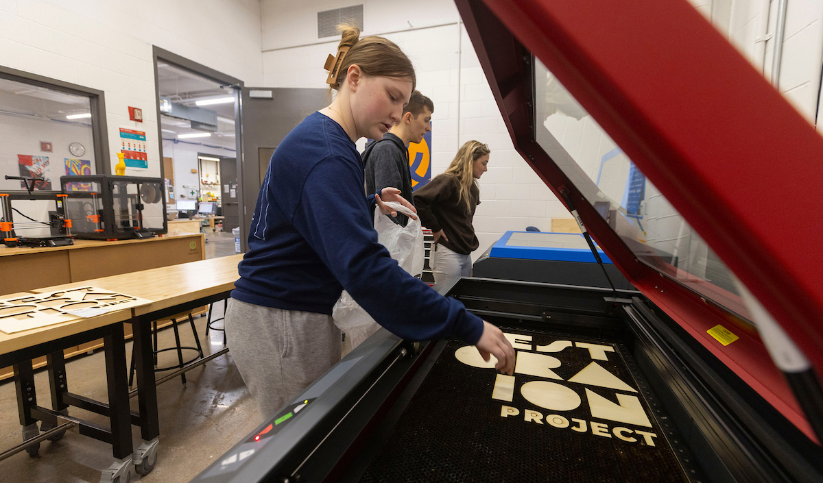 A female student removes laser-cut wood letters from a laser cutter.