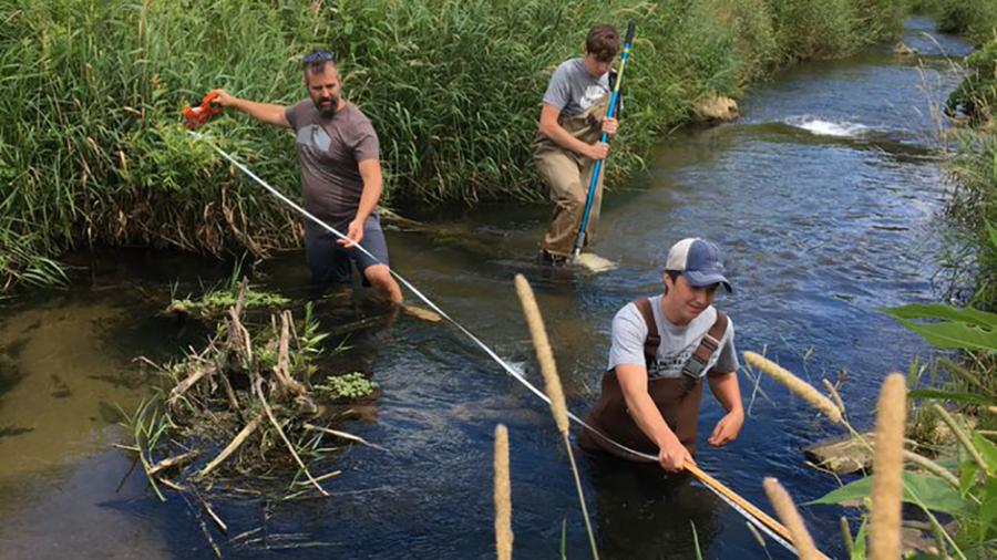 Keith Gilland, left, Kal Breeden, foreground and Dylan Kostuch measure stream width this summer as part of their research.