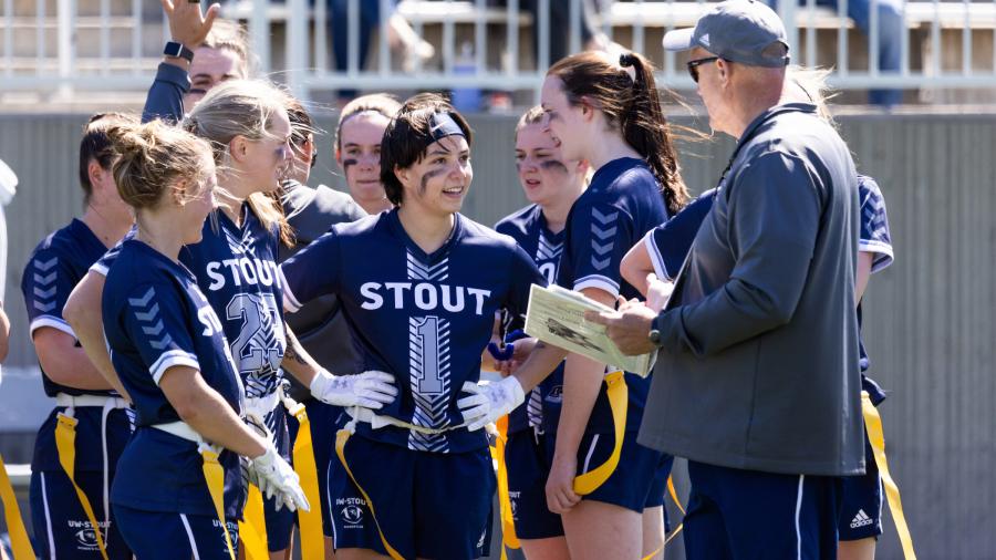 Coach Duey Naatz speaks with players on the sidelines during the inaugural Midwest College Women’s Flag Football League Championship.