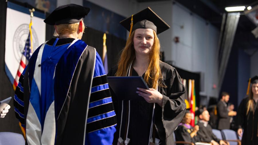 A student crosses the stage at commencement to receive their diploma.