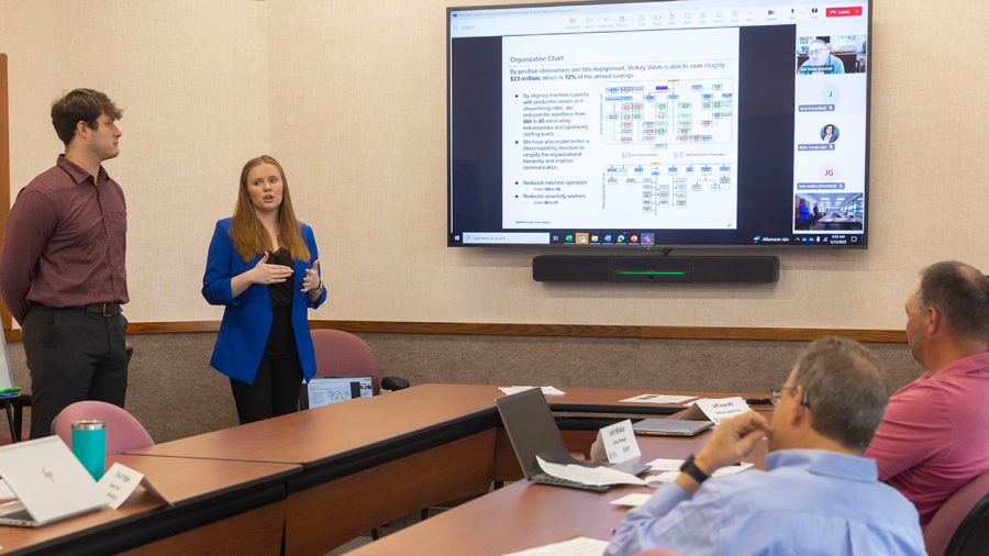 Two supply chain students present their capstone project in a corporate boardroom to a group of industry professionals.