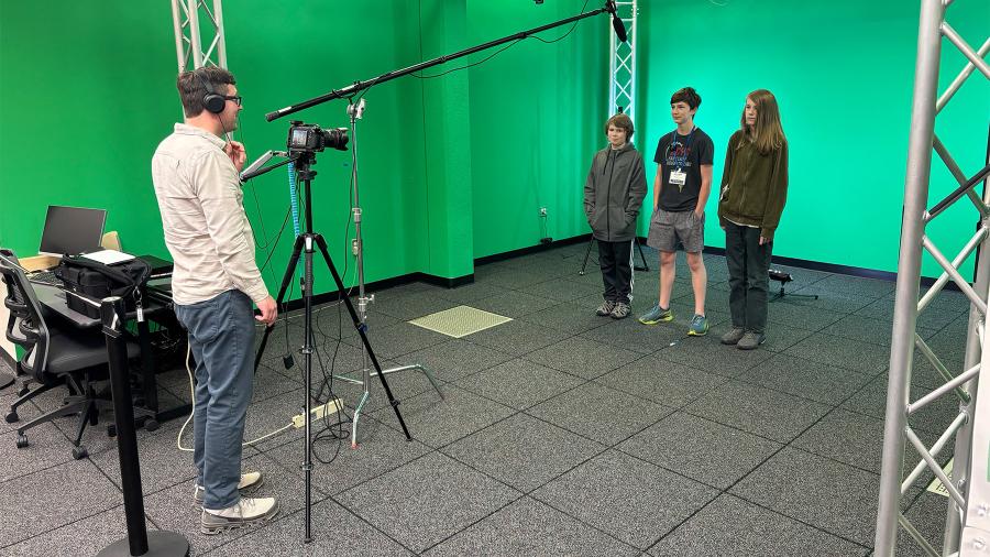 A professor and three students film video in from of a green screen