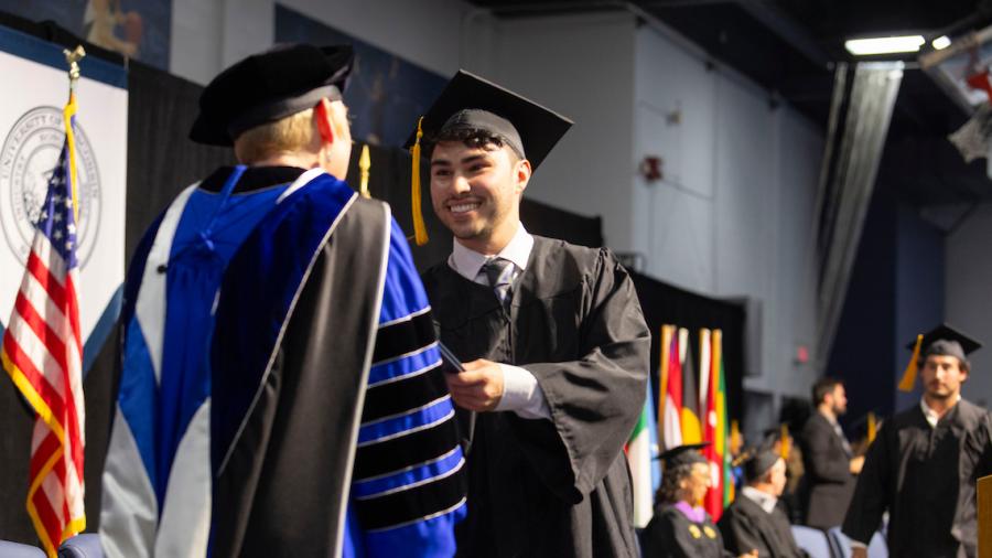 A student receives their diploma from Chancellor Frank