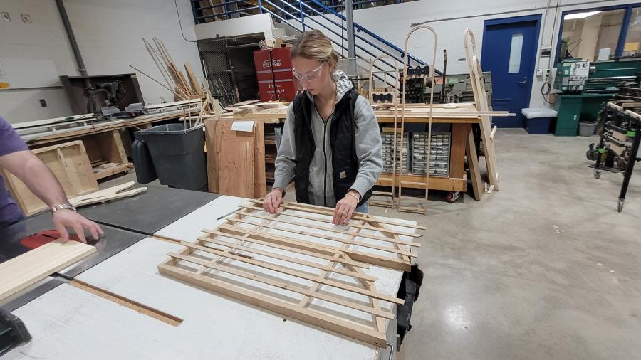 An industrial design student evenly spaces slats on the frame of a show rack.