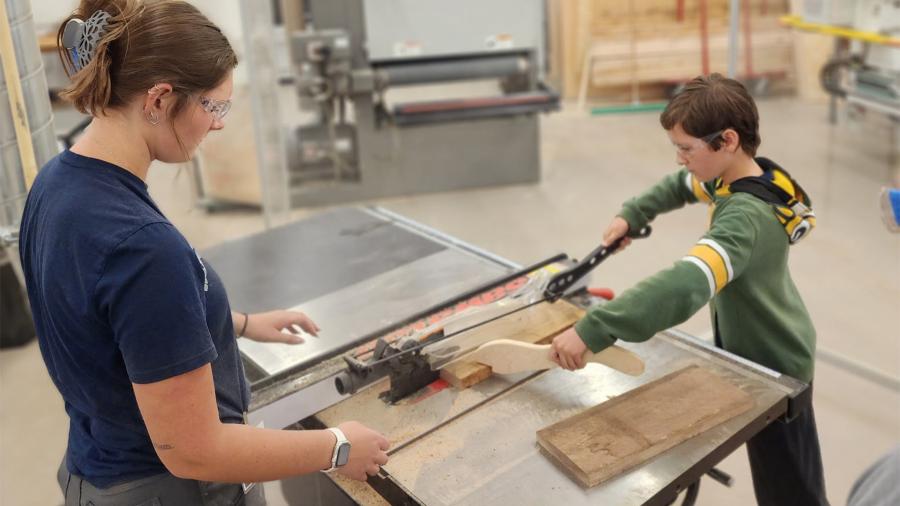 STEAM Construction camper and instructor cutting a piece of wood on the table saw