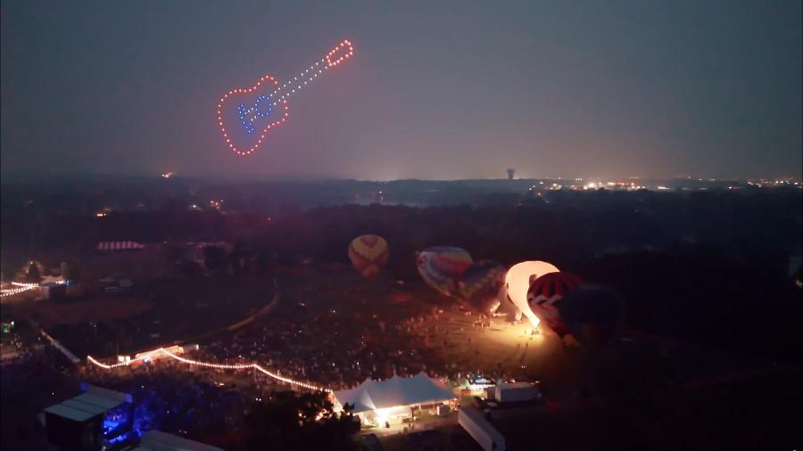 Illuminated drones form a guitar shape in the sky above a hot air balloon festival