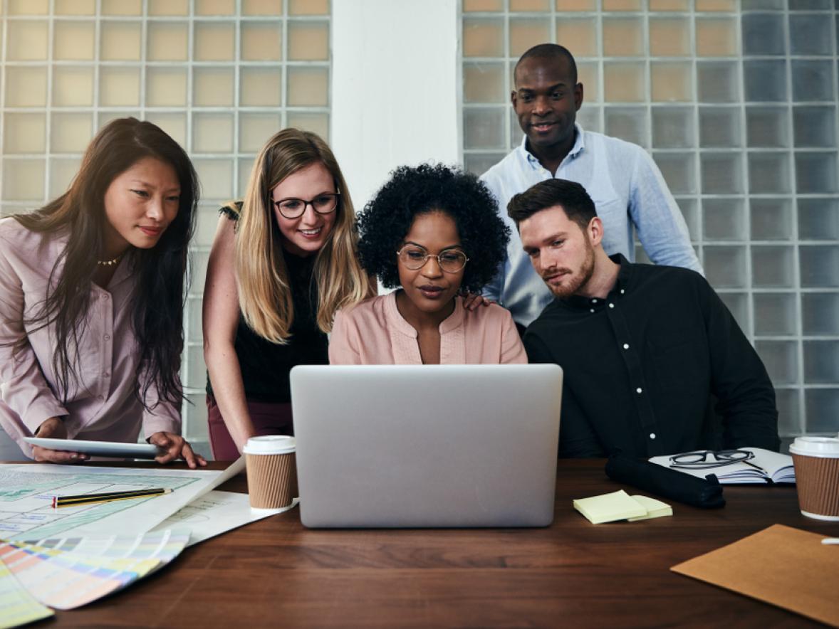 Photo of a group of adults gathered around a laptop