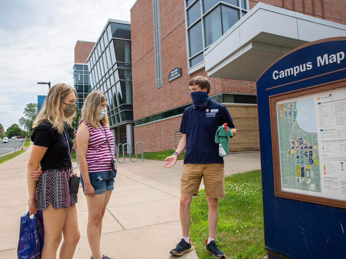 An Admissions Office guide wears a mask and carries sanitizer spray while conducting a tour for new students at UW-Stout.