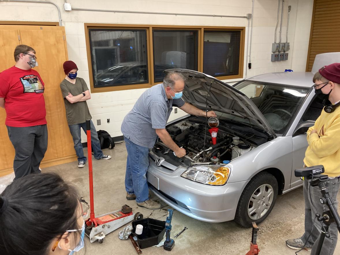 UW-Stout’s Student Centers Director Darrin Witucki adds oil to car he was working on during an Adulting 101 series.