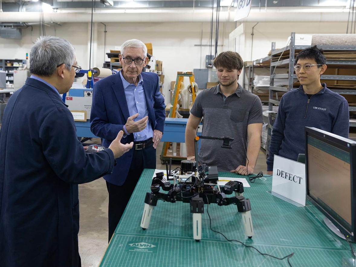 Professors David Ding, left, and Yuan Xing, right, and engineering student Michael Witt explain an AI-developed robot to Gov. Evers.