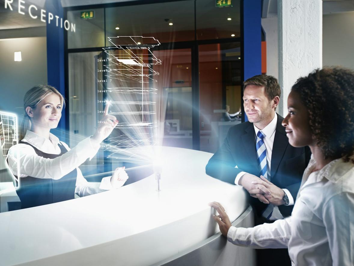A concierge uses a generative AI hologram to address the needs of two guest at a hotel's front desk..