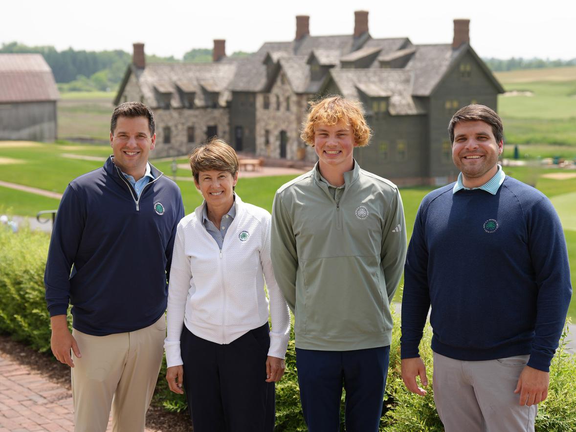 Four people stand outside a golf club house