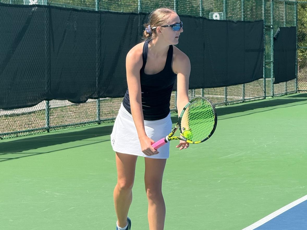 UW-Stout tennis player prepares to serve during a match on an outdoor court at the USTA National Campus.