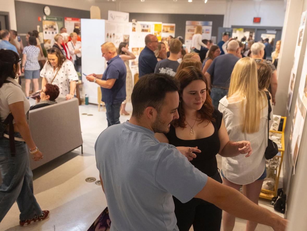 Two students admire a work of art, while in the background a sea of people review various installations and exhibits at UW-Stout Polytechnic's School of Art & Design Senior Show.