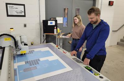Packaging students Abbey Dahlseng and Ben Lindgren at the Kongsberg digital cutting table
