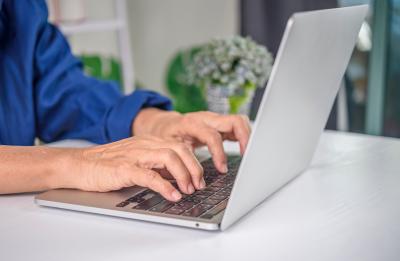 A person typing on a laptop at a white desk with a small potted plant in the background
