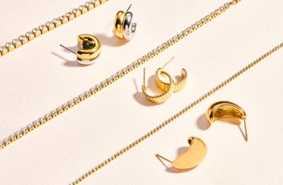 Gold and silver earrings and gemstone chains arranged on a light-colored surface for a jewelry product display.