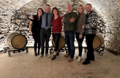 Dave Rasmussen poses with family members inside a stone-walled wine cellar with wooden barrels in the background.