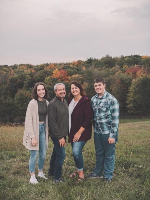 Four family members pose together in a grassy field with autumn trees in the background.